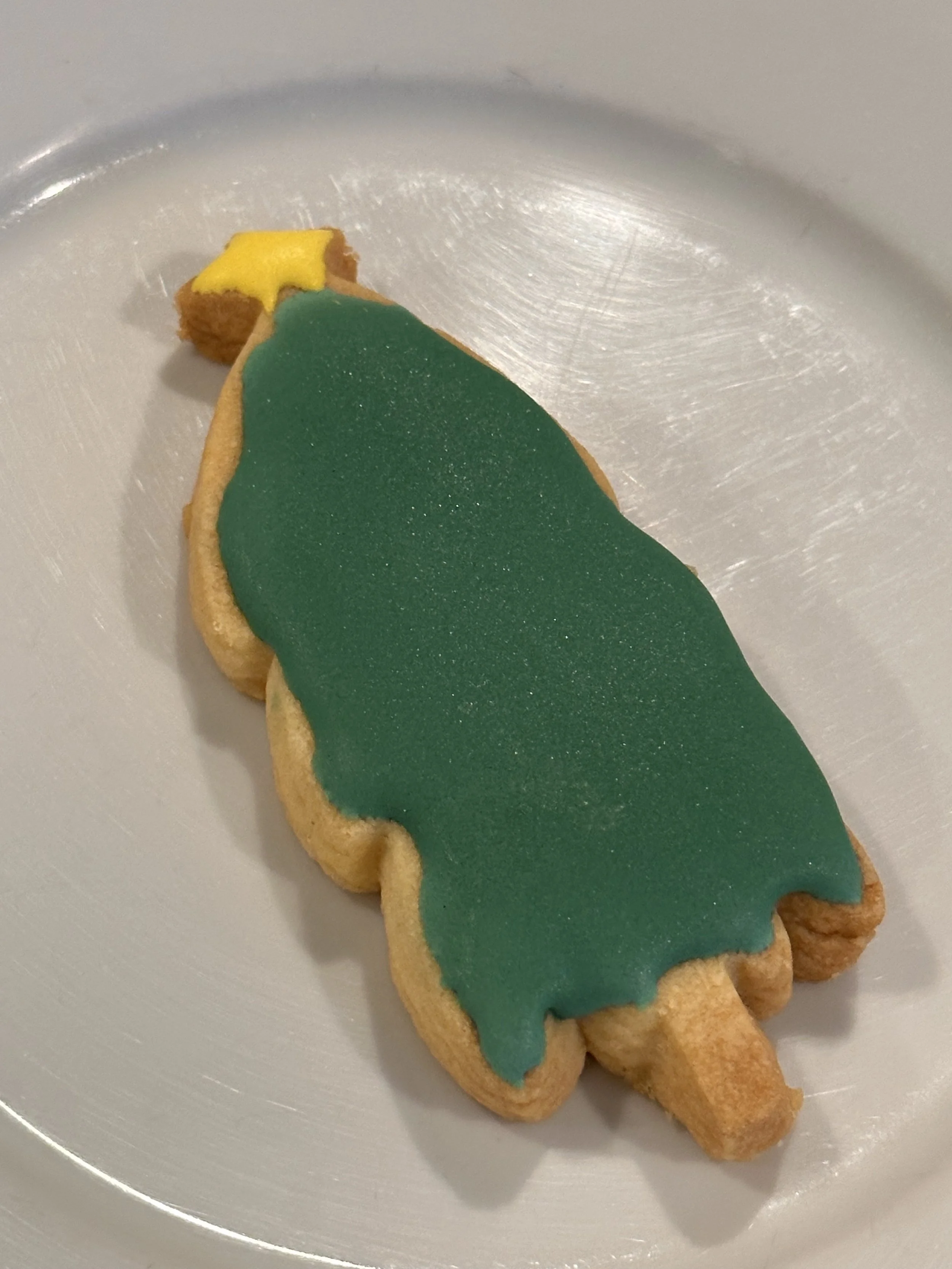 A Christmas tree cutout cookie with green icing and a yellow star, quite average in appearance
