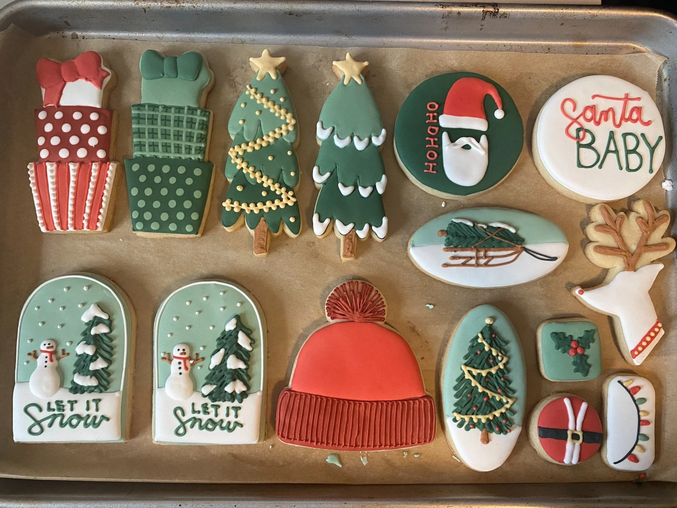 A variety of shapes of Christmas cookies, beautifully decorated with rich colors of green, red, and white. Shapes include Christmas trees, reindeer, a hat, and snow globes